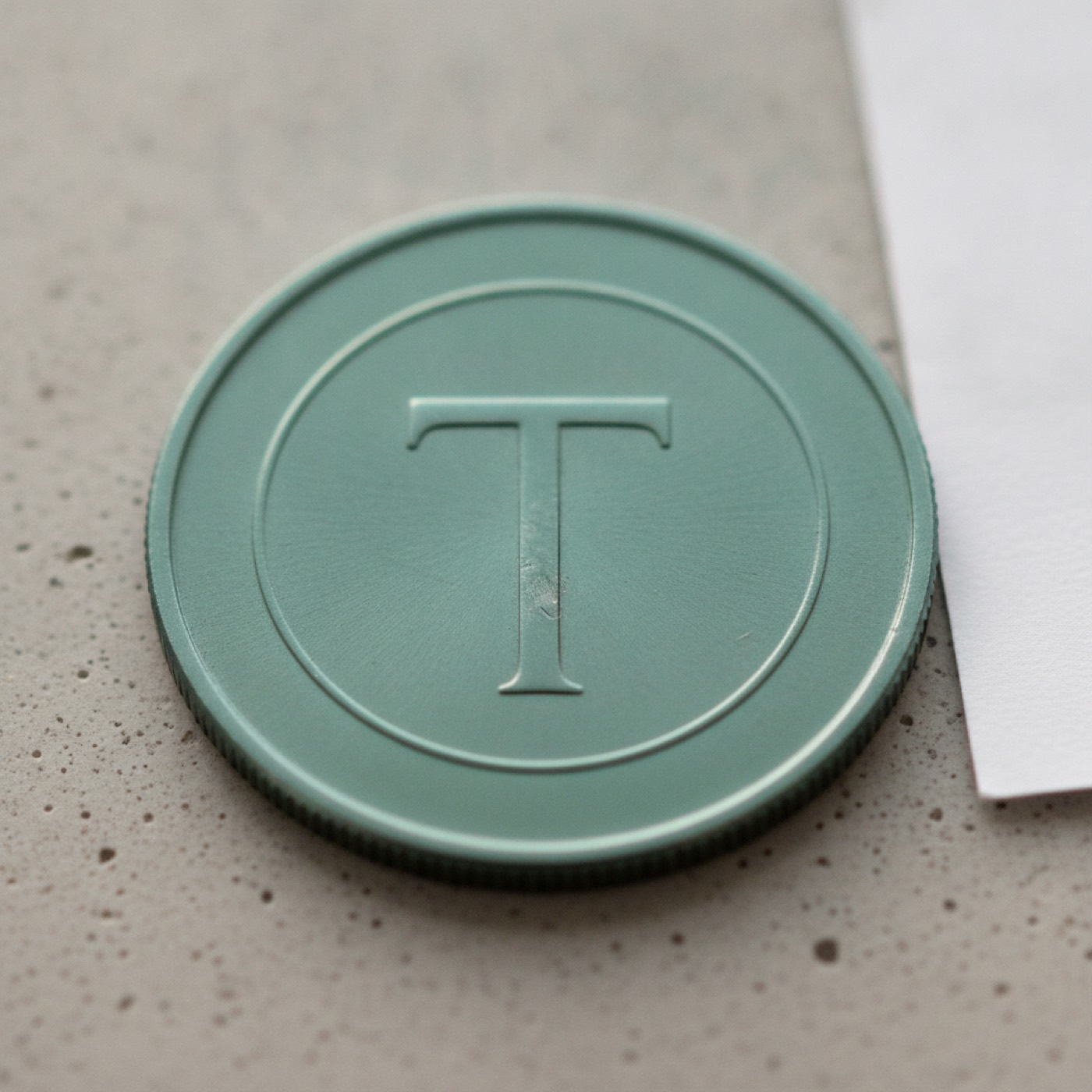 A single Tether coin photographed on a pale concrete slab